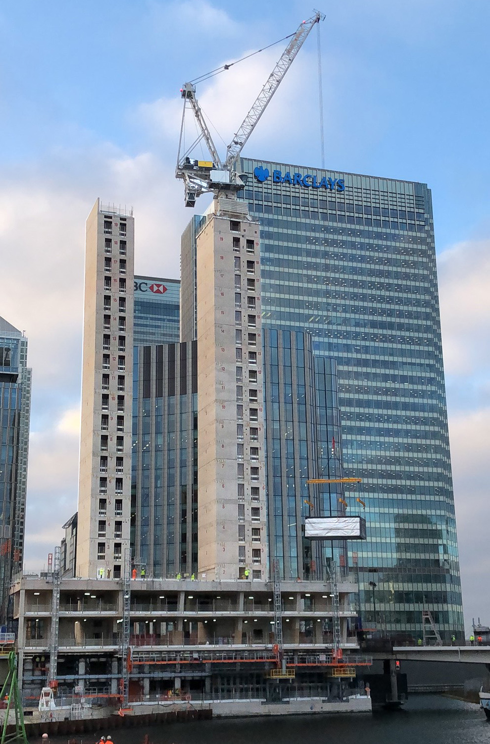 B2 Building Wood Wharf under construction with exposed cores towering towards the blue sky, which has little fluffy clouds puffing up behind the rooftop crane