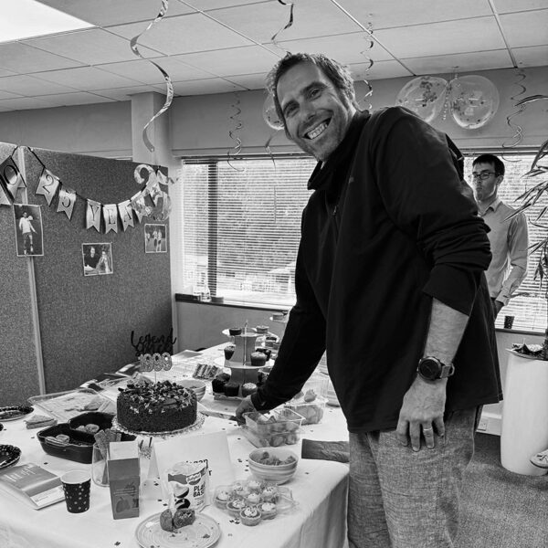 Black and white photo of a man cutting his work anniversary cake at a table