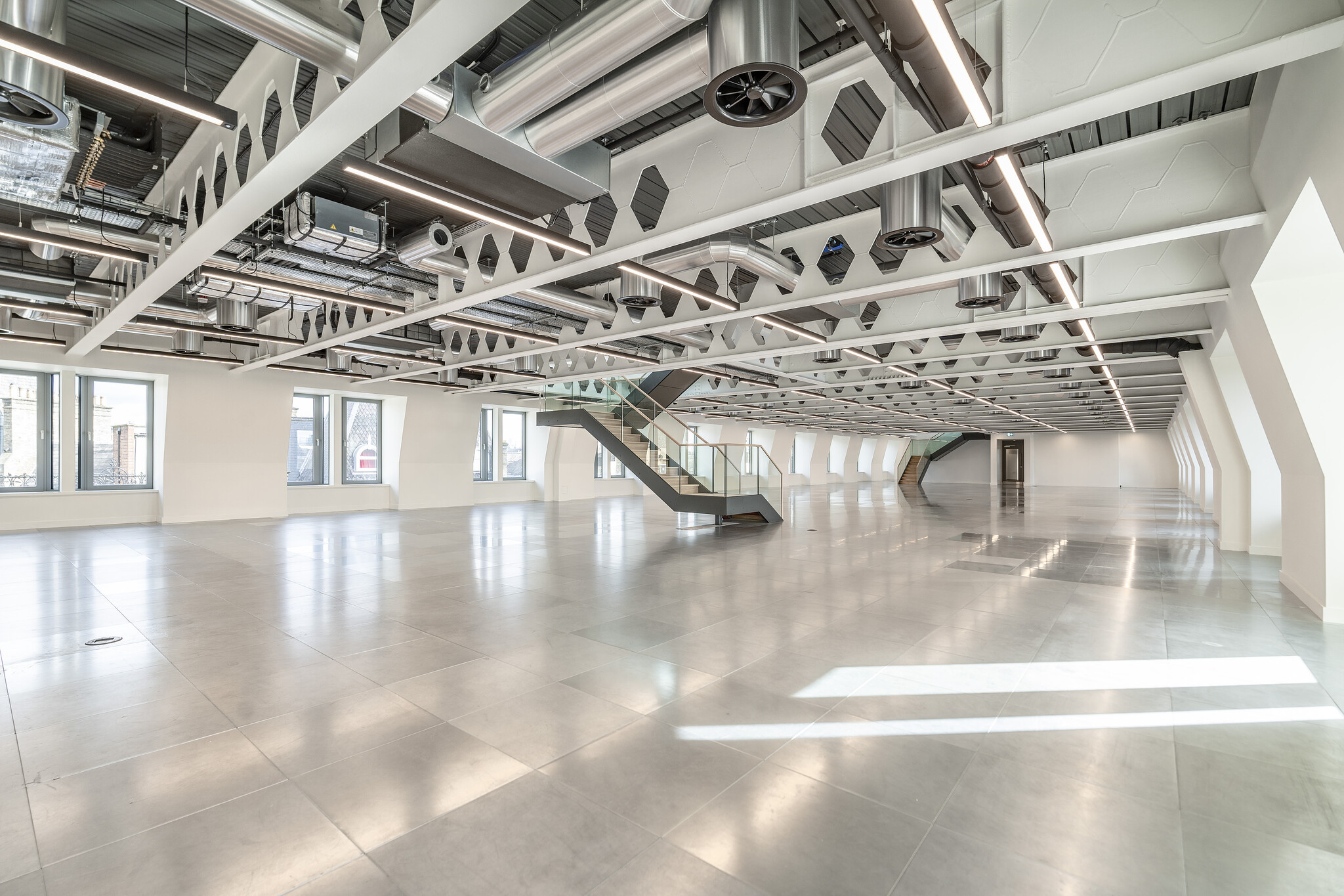 Minimalist office interior with polished floor, white walls and punched steel beams overhead, also a single stair case