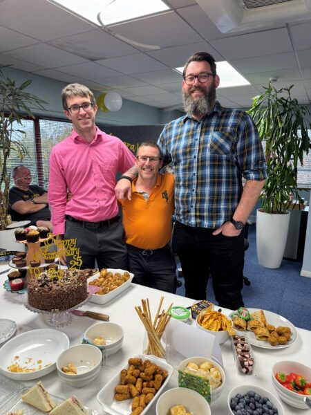 Cambridge structural engineers and technicians celebrate their work anniversaries around a spread of food and cake