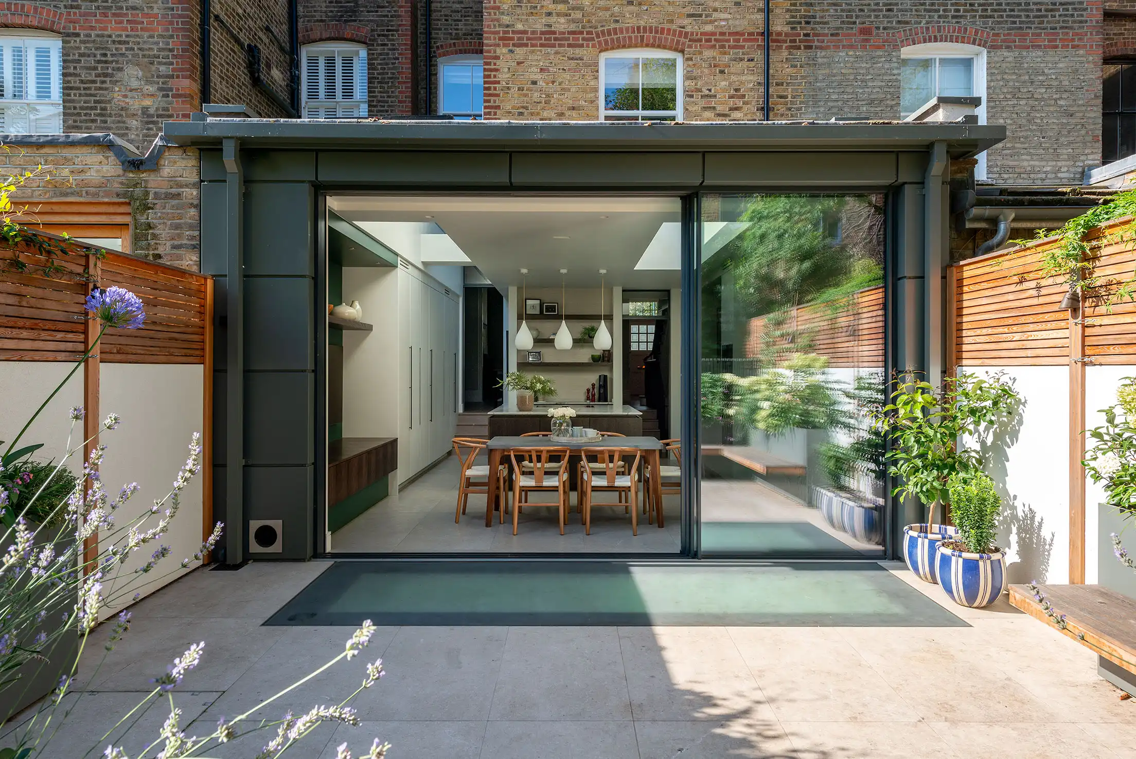 Rear garden extension with glass sliding door looking into contemporary white kitchen