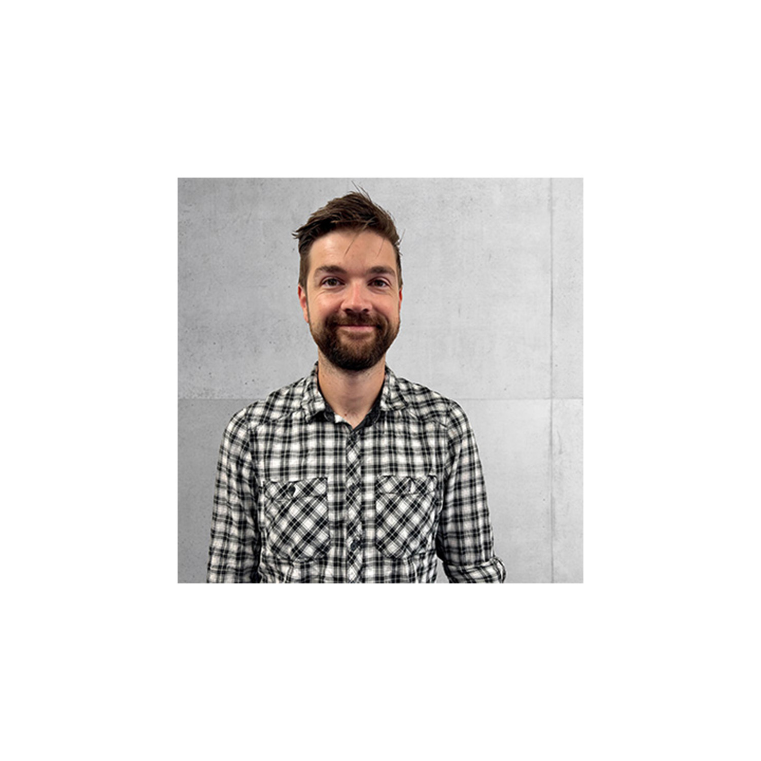 Young man with dark hair and beard wearing gingham shirt in black and white for Peter Dann Engineers Cambridge team