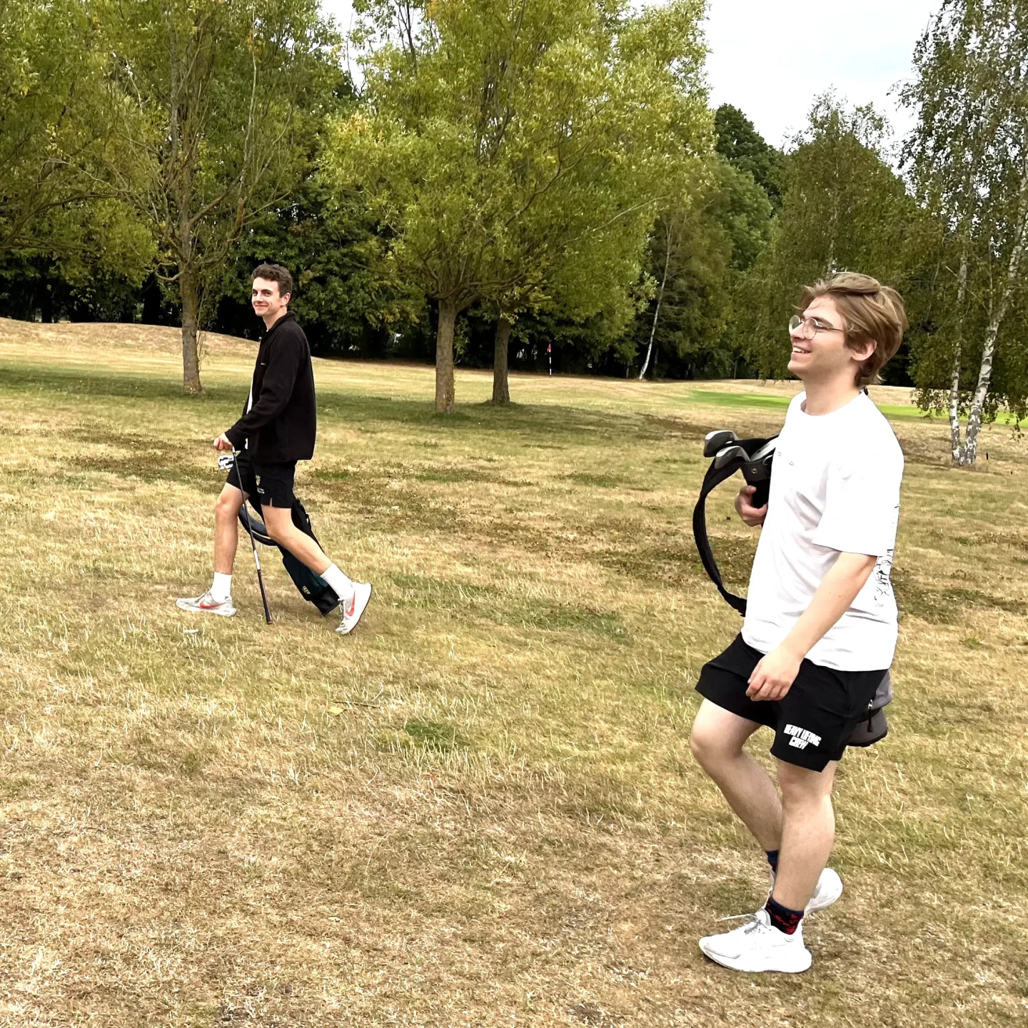 two young men walking with golf clubs and bags through the course