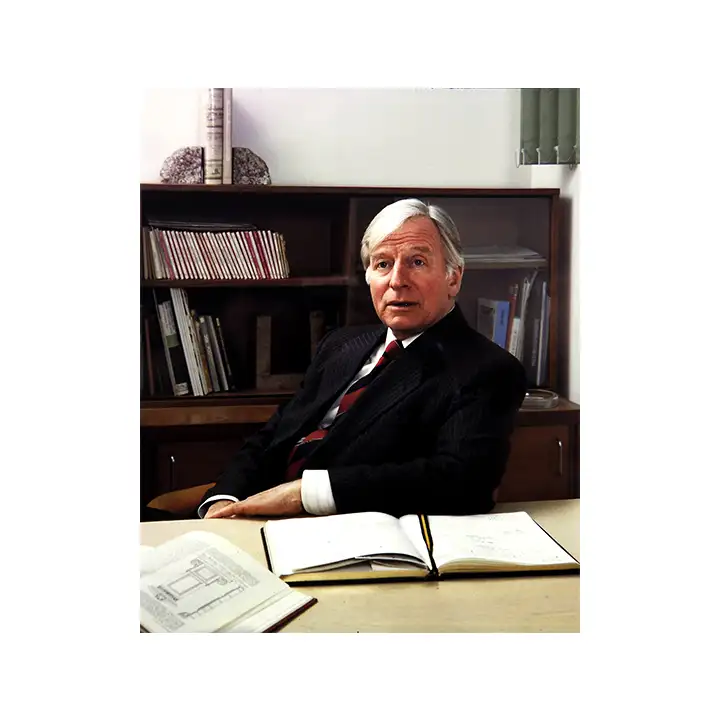 Peter Dann Founder in suit behind large desk 1980s